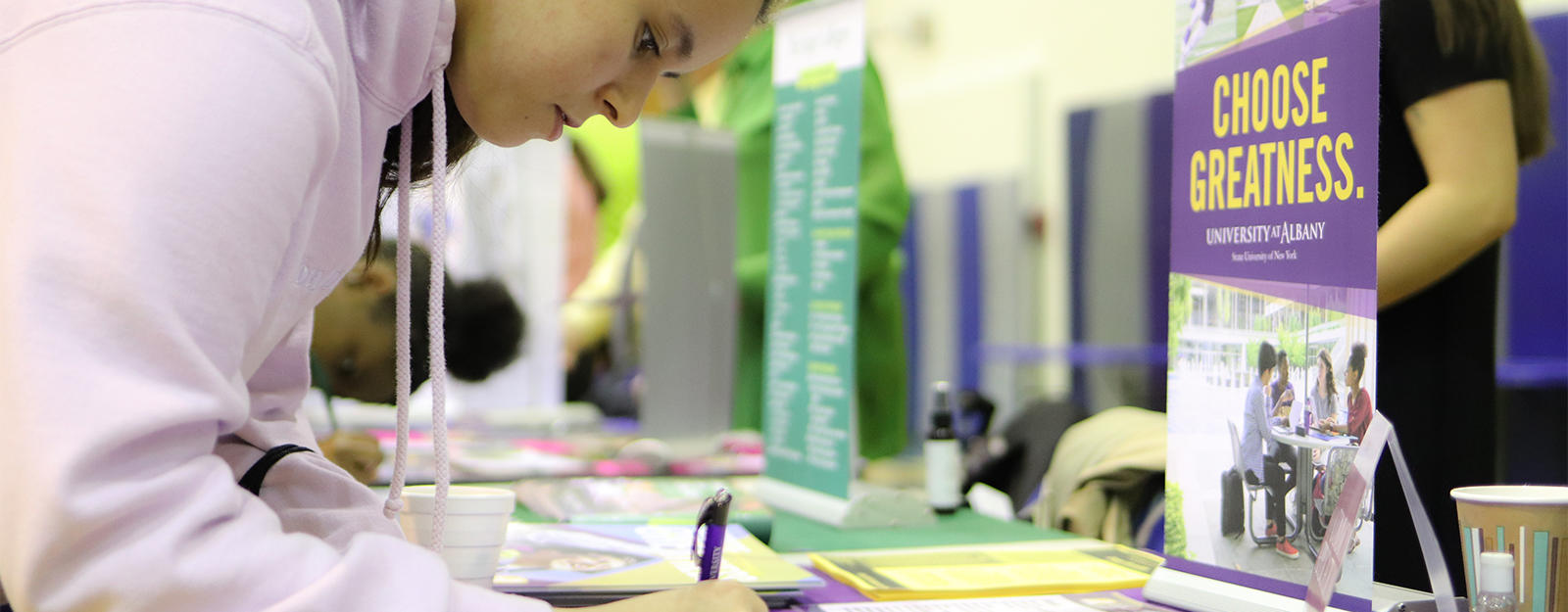 Student filling out paperwork at a SUNY ʿ table during a college fair.