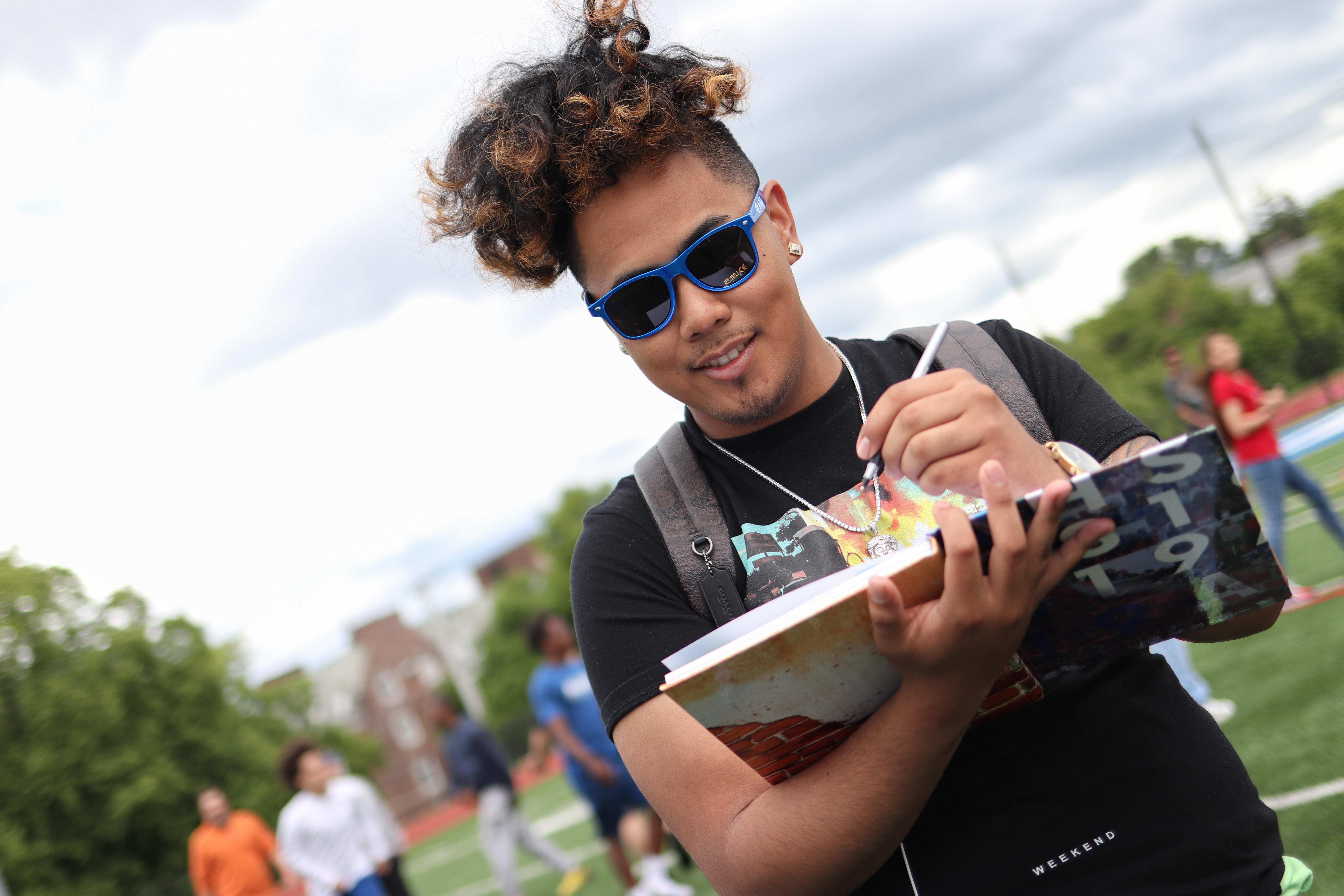 Male student signing on yearbook on ʿ High's turf field.